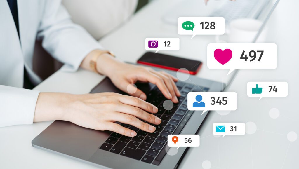 Hands typing on laptop with social media icons.