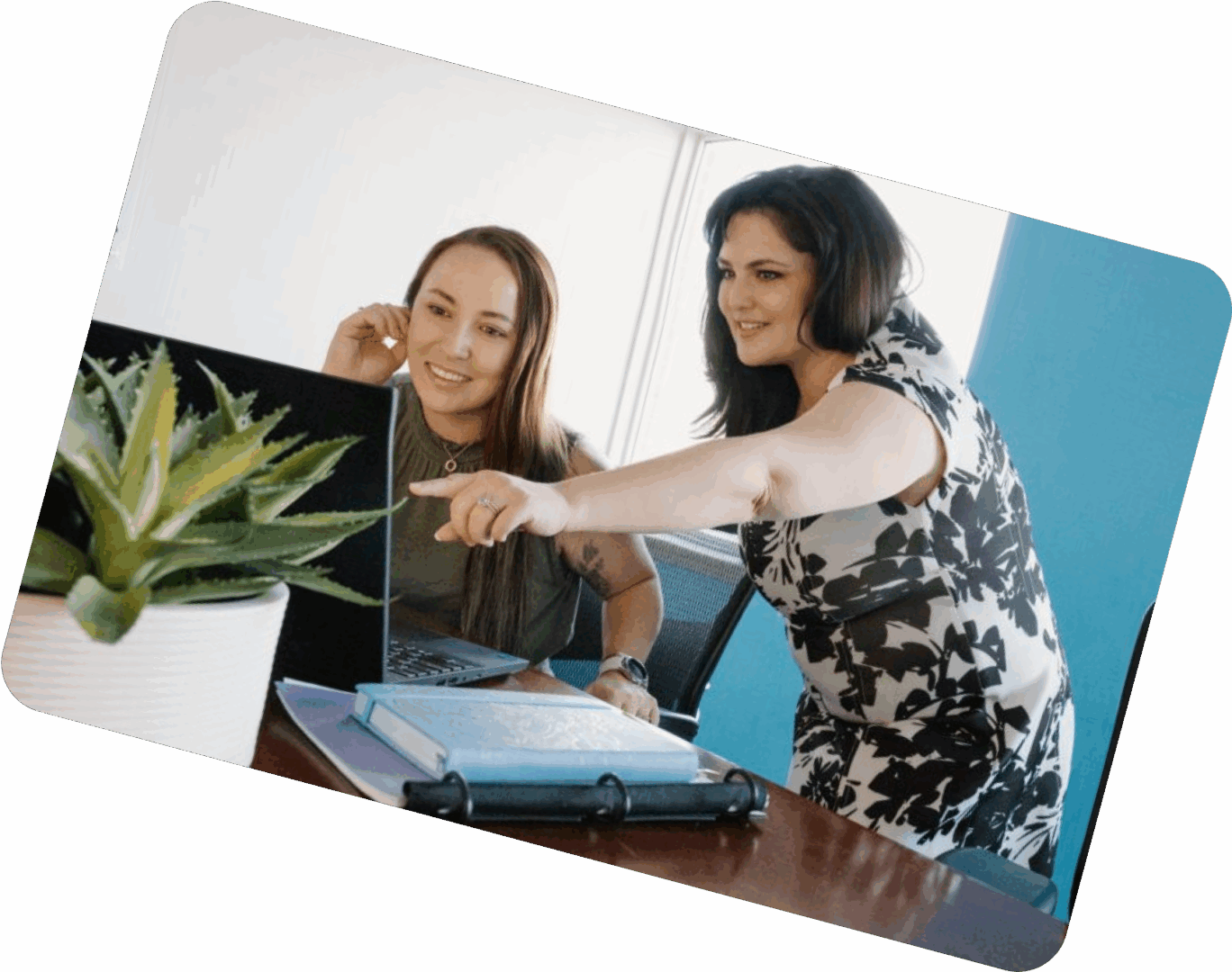Two women collaborating over a laptop and documents at a desk.