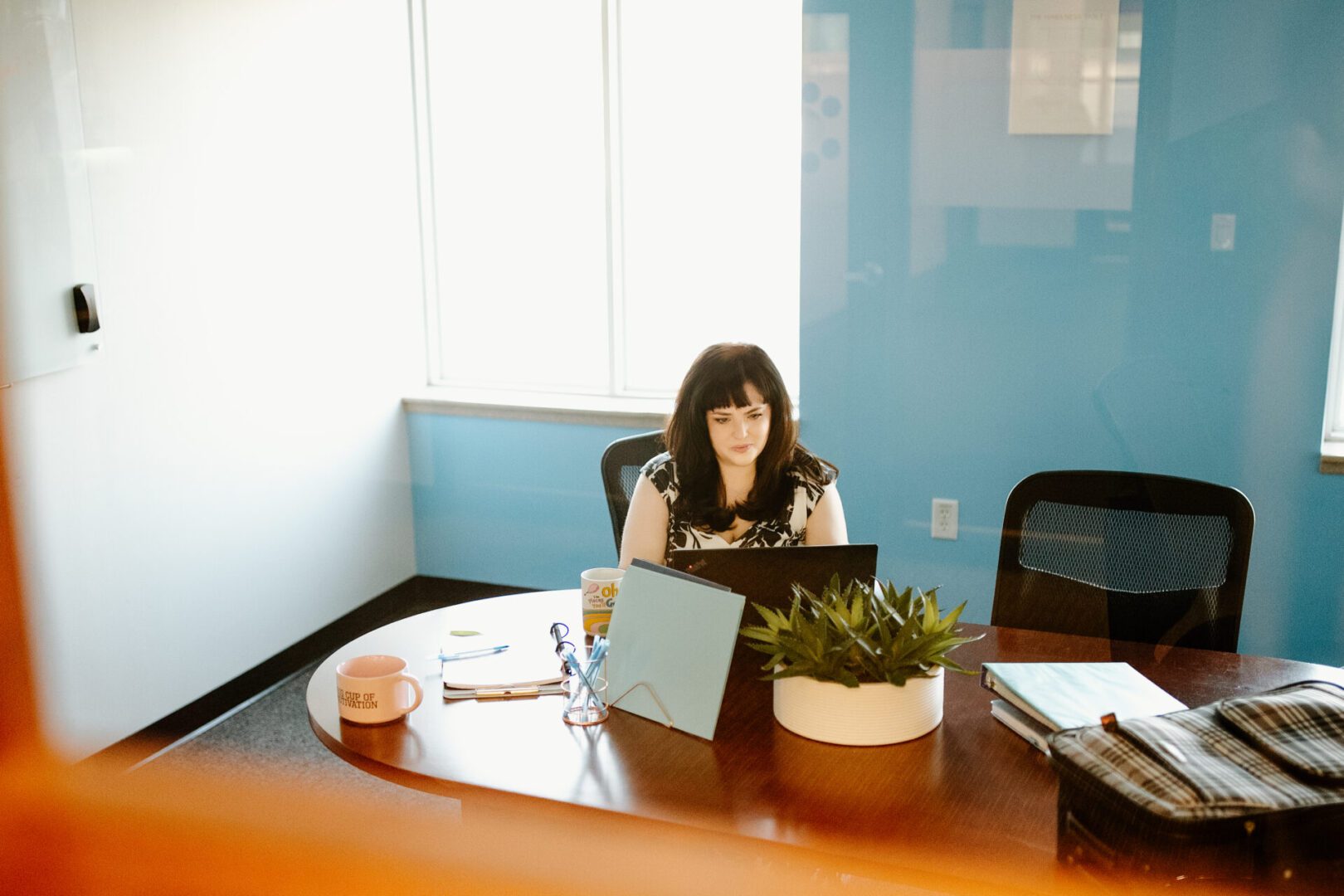 Woman working on laptop at a round wooden table in a bright office.