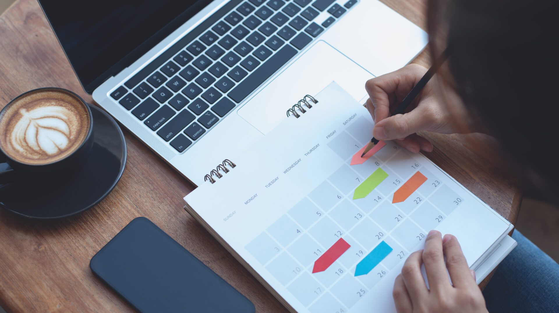 Person marking dates on a calendar beside a laptop.