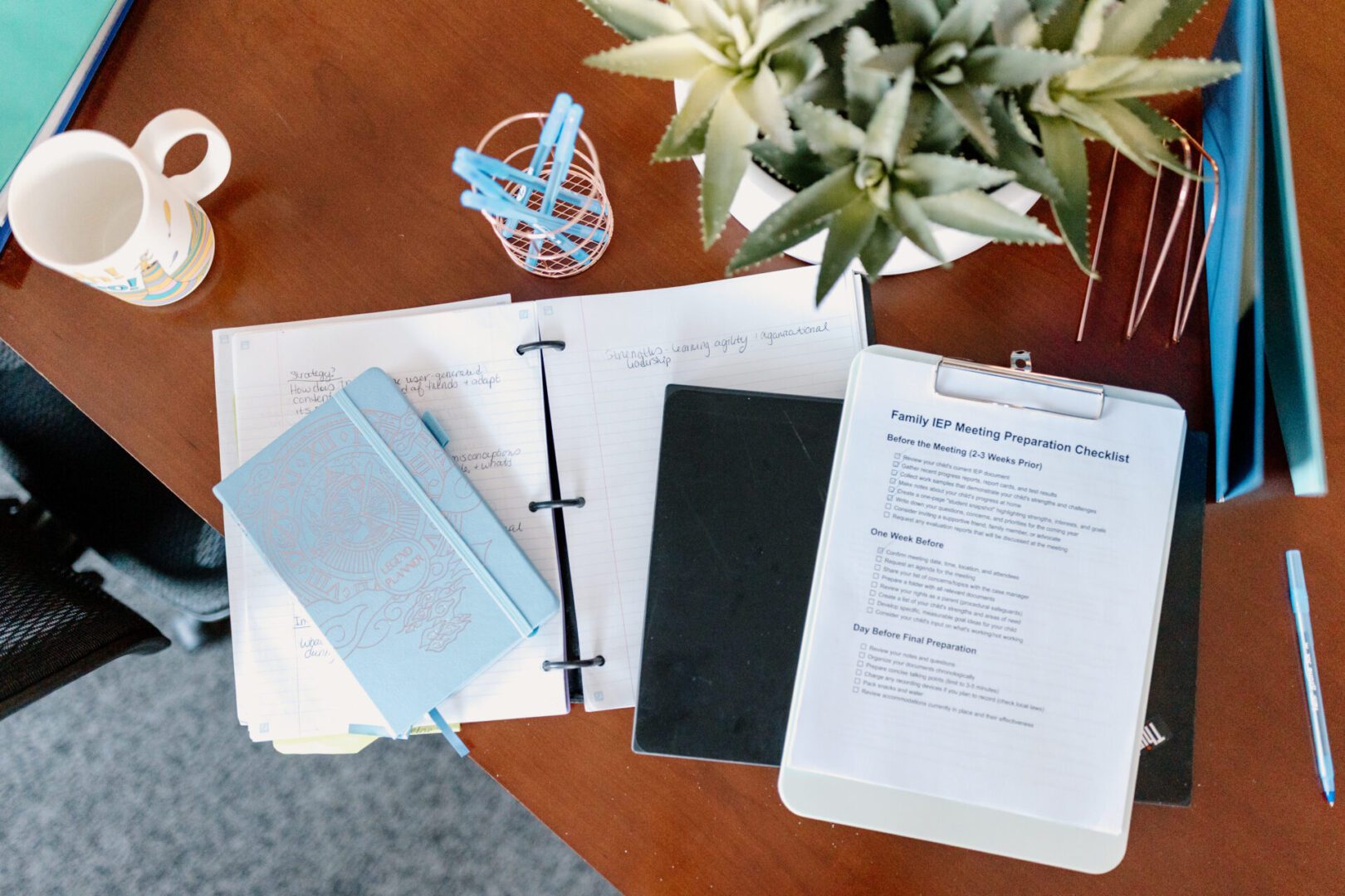 Documents, a pen, and a paper crane on a wooden desk with white flowers.