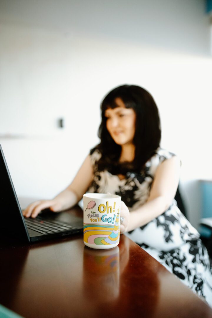 Woman using a laptop with a container of Oh! Go! powder on the table.