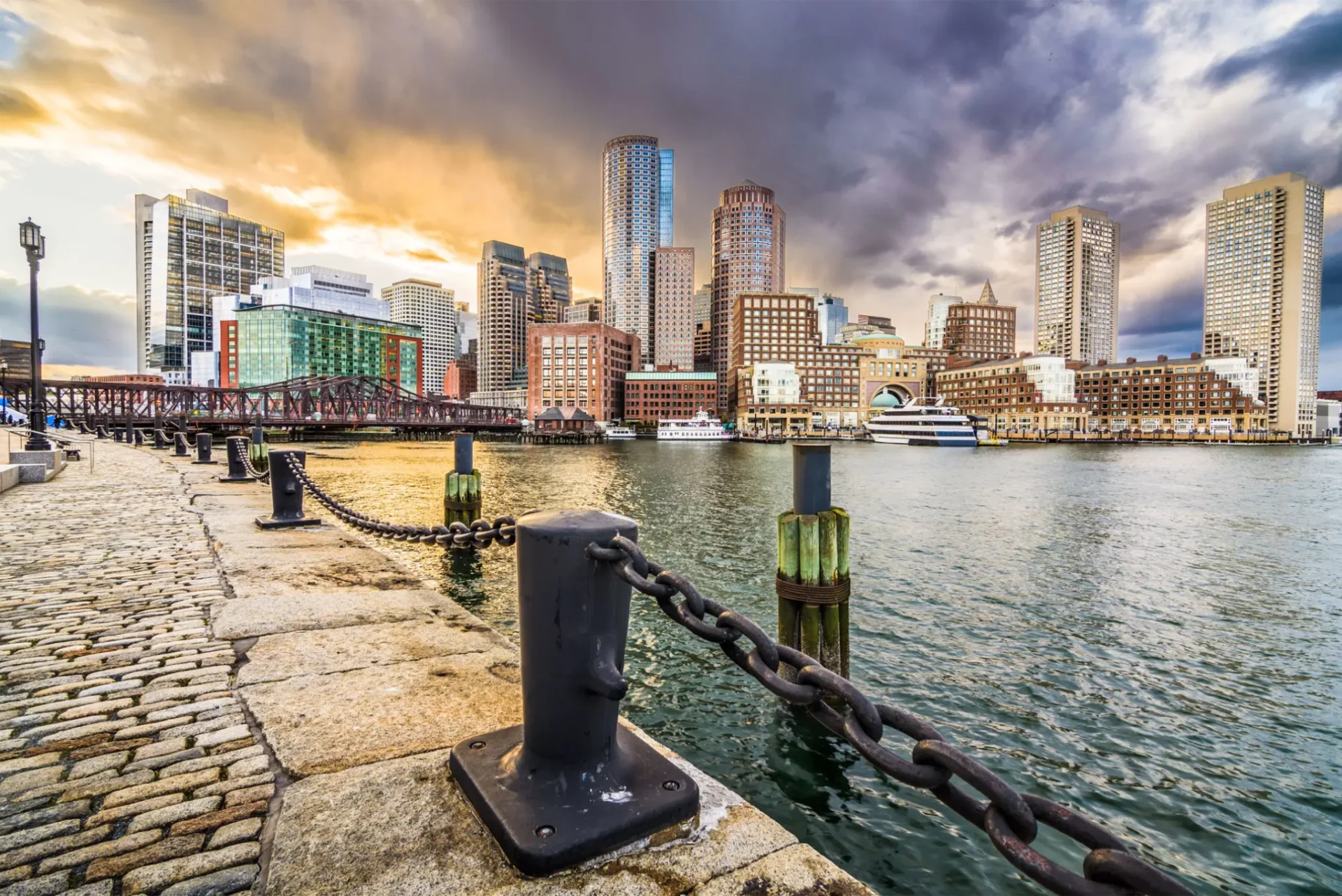 Sunset view of a city skyline across a waterfront with mooring chains.