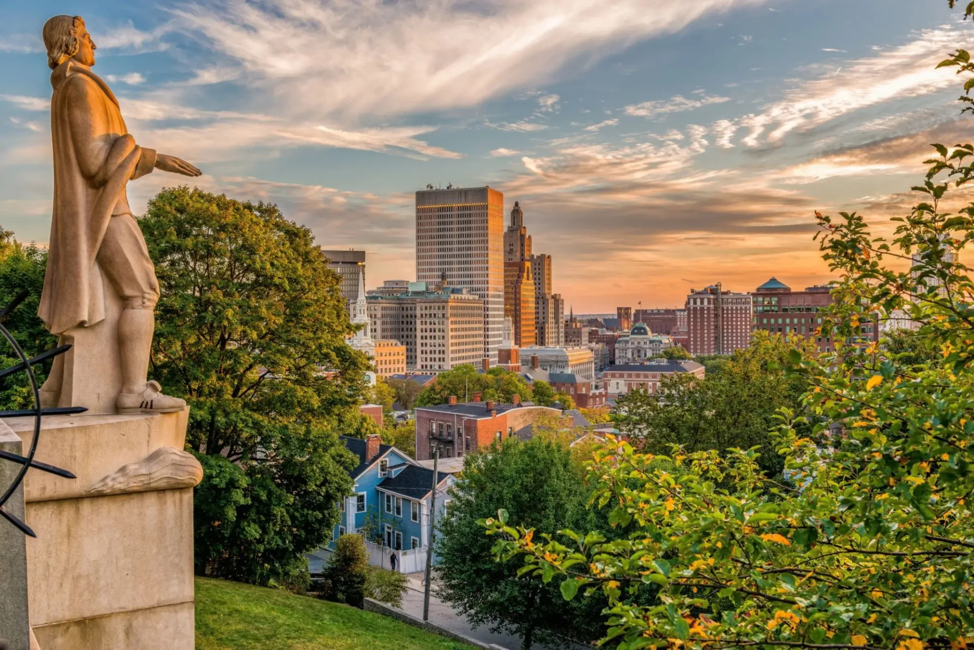 City skyline at sunset with lush greenery in the foreground.