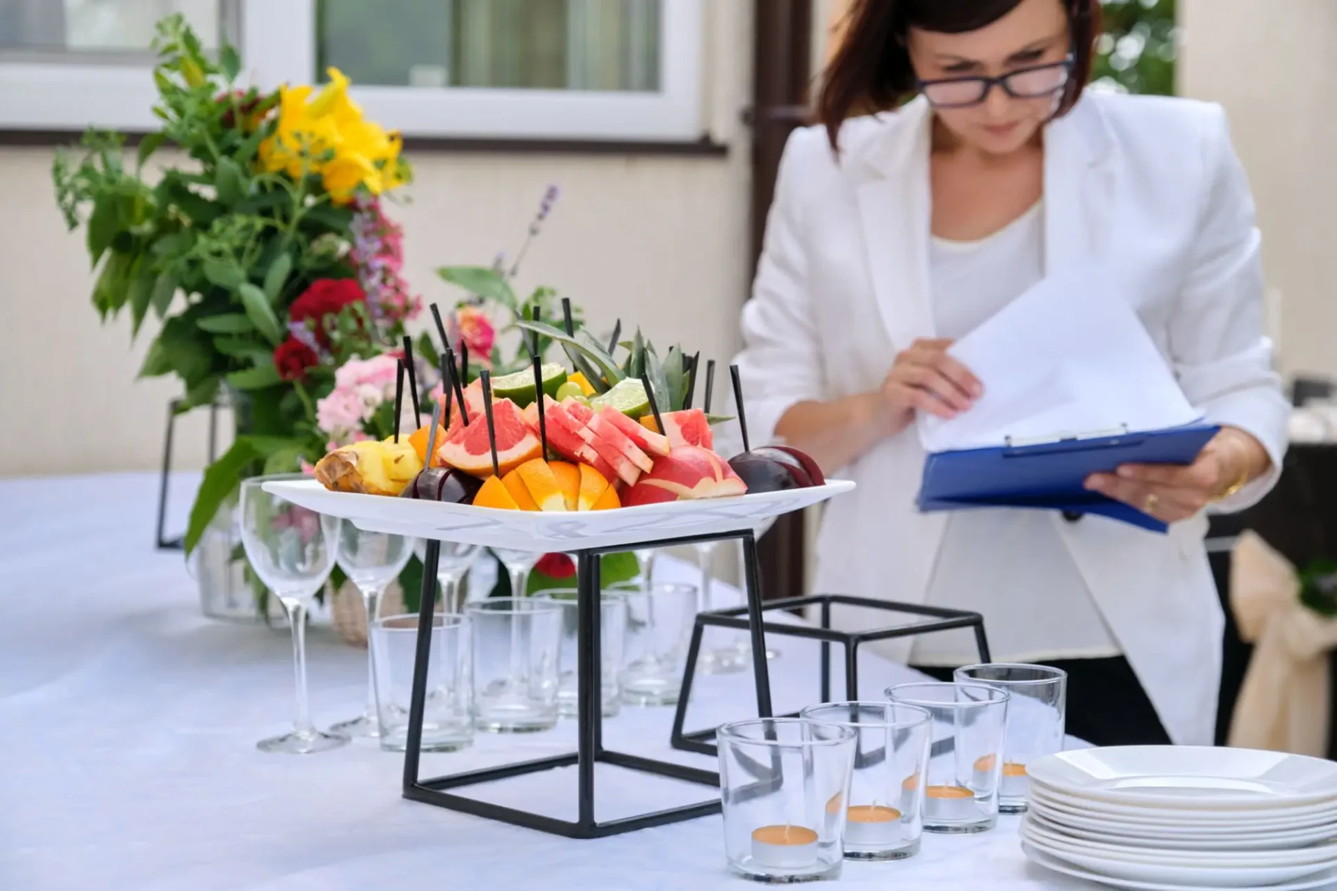 Fruit skewers served on glasses at an event with a woman in the background.