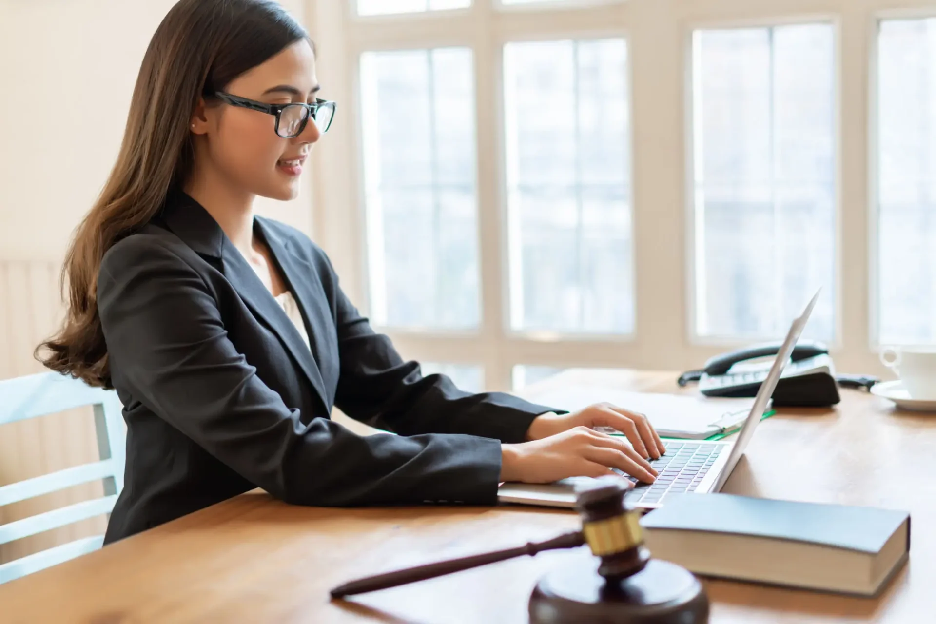 A female lawyer working on a laptop with a judge's gavel nearby.